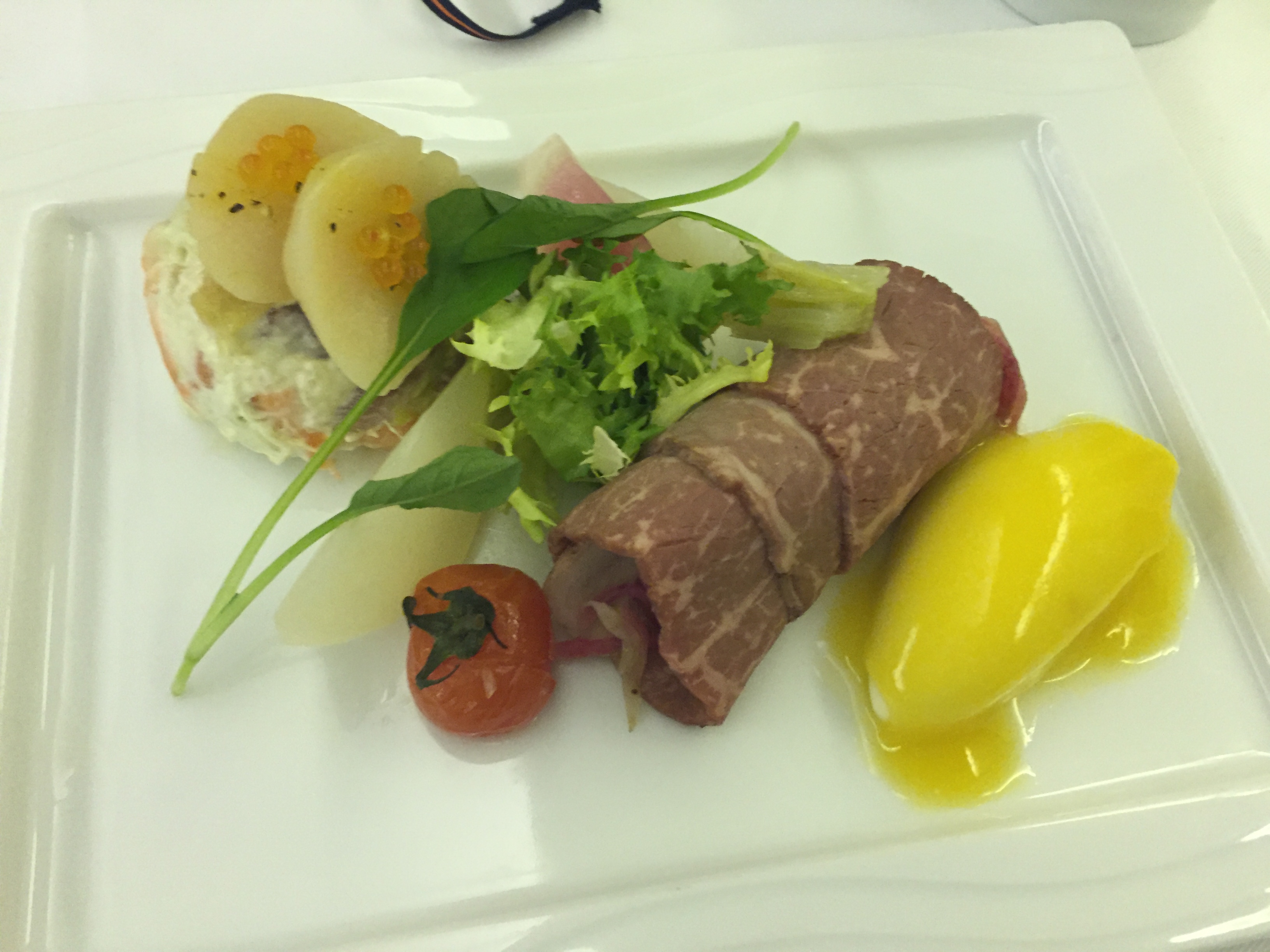 A sliced beef roulade wrapped around vegetables, with potato gratin, salmon and ikura, frisée salad, and mango sorbet