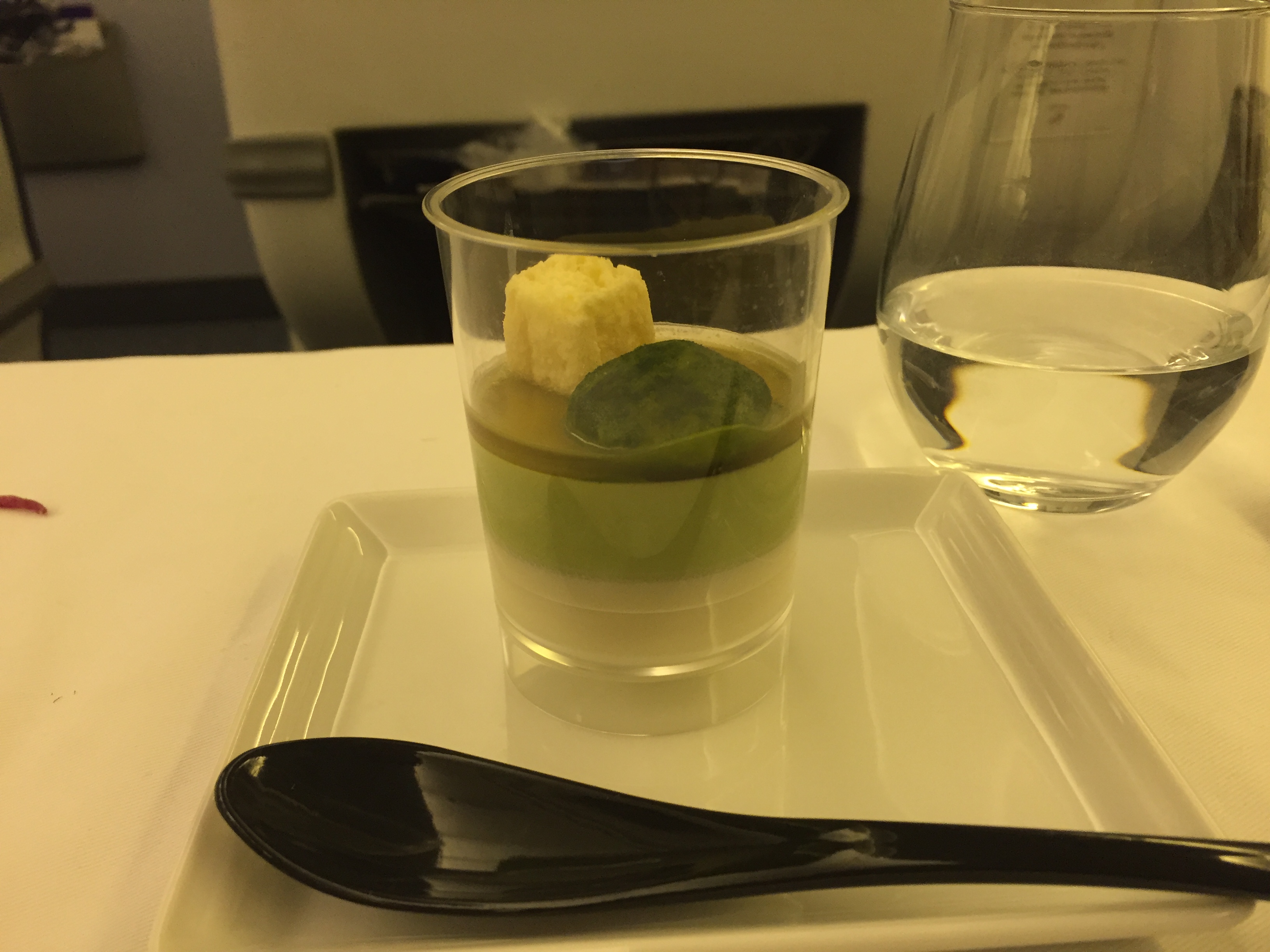 A layered dessert — clear yuzu jelly with a green matcha layer, topped with a mochi cube and shiso leaf
