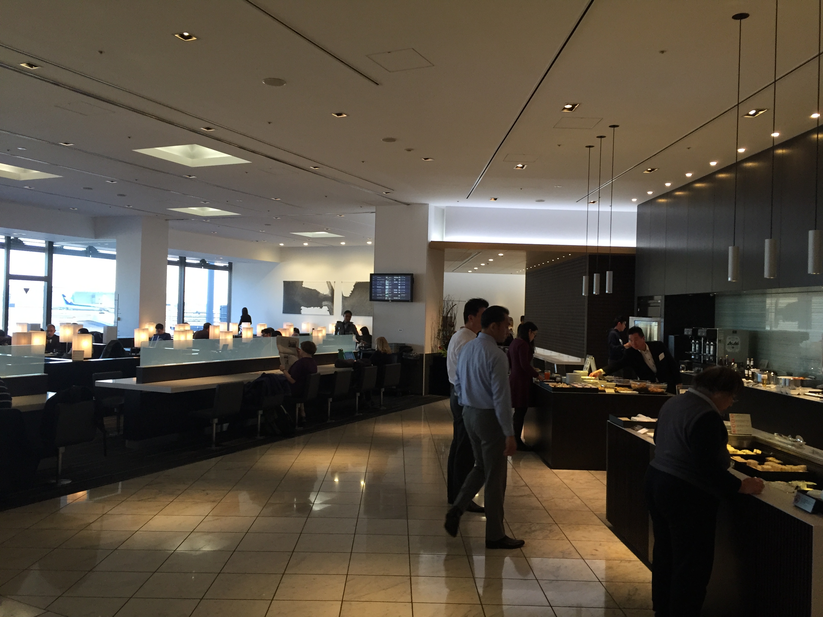 The ANA business lounge interior at Narita — modern space with a buffet on the right, dim lighting, and runway views