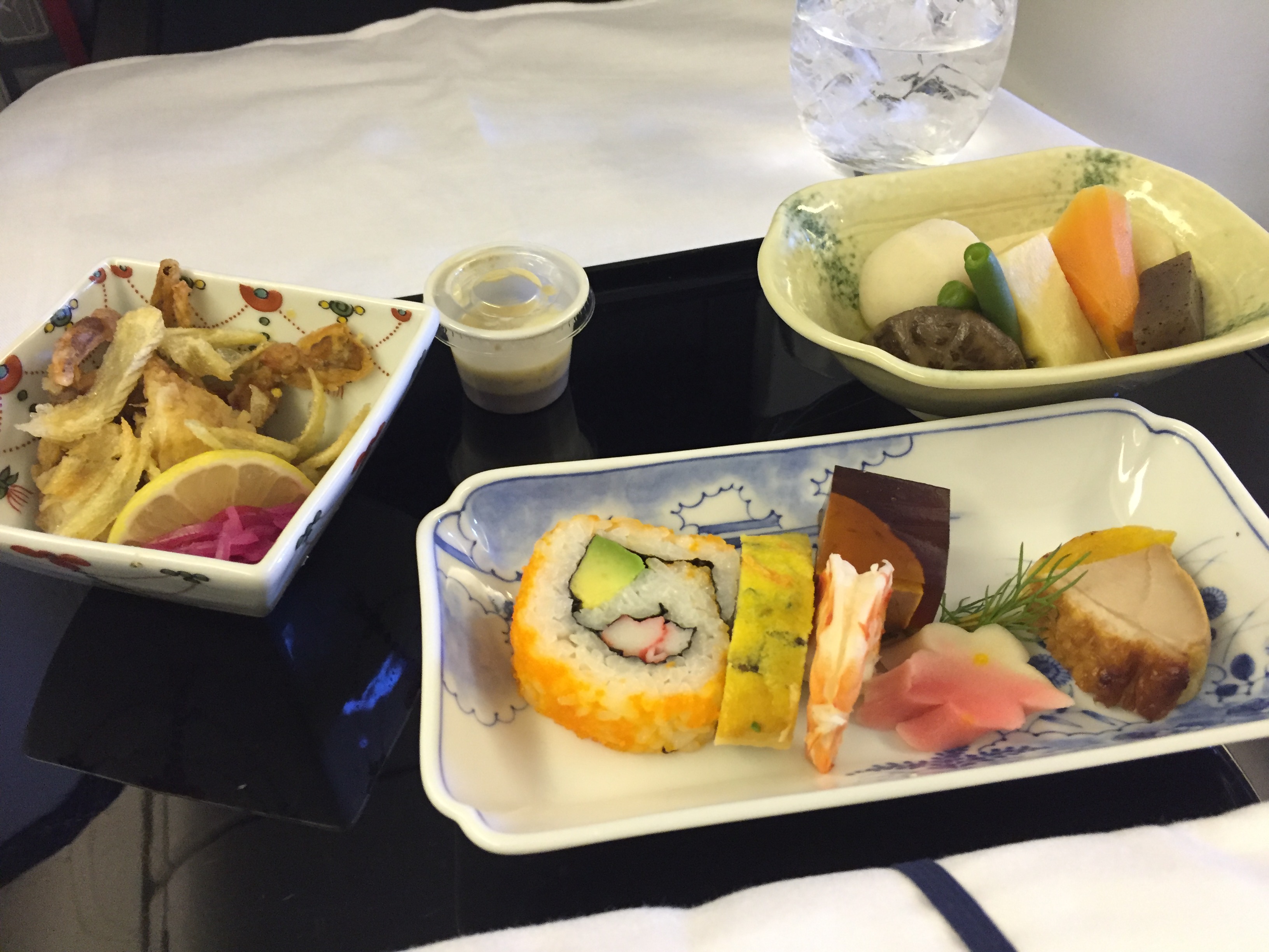 A bento-style plate with a sushi roll, tamagoyaki, simmered vegetables, and tempura on the side