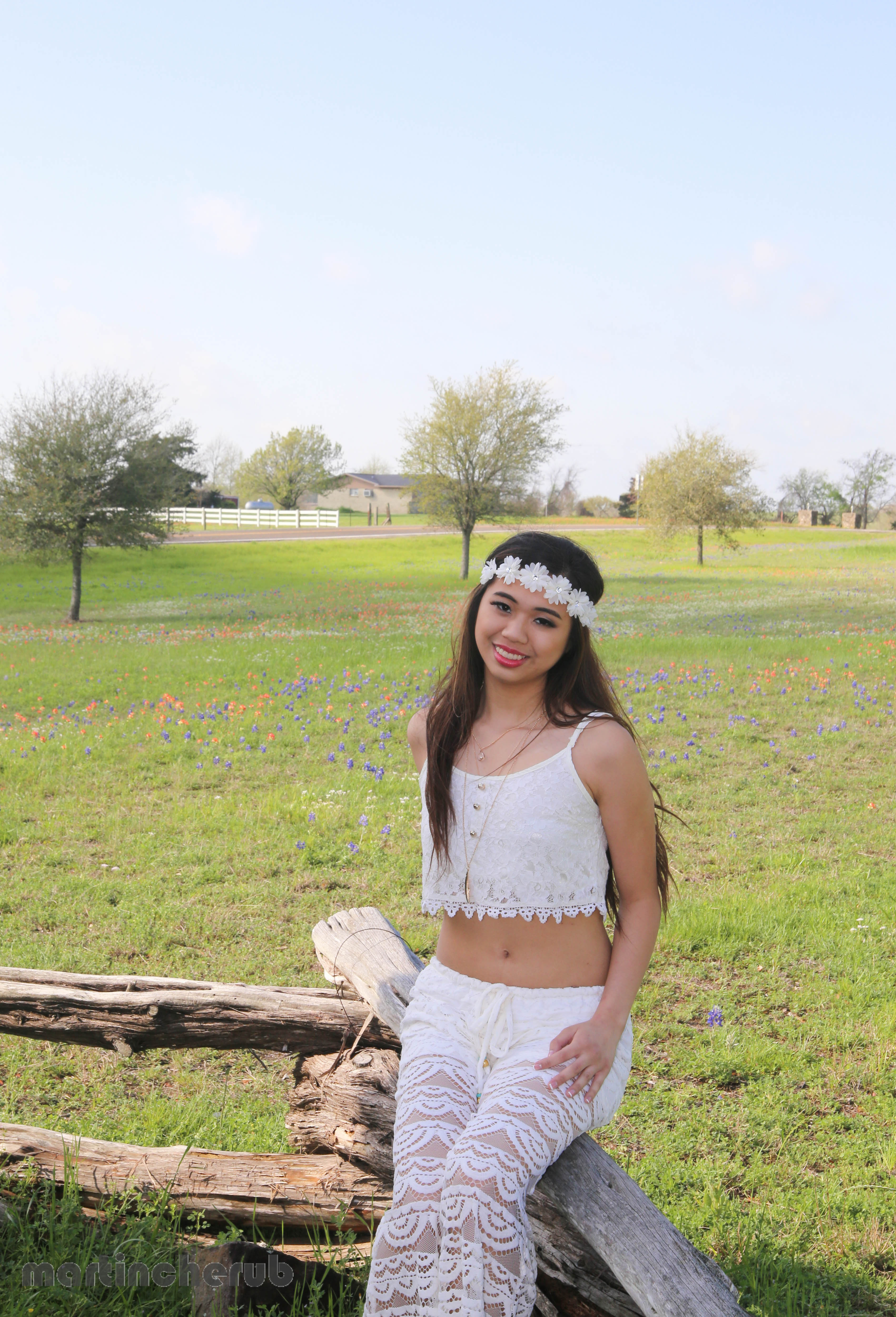 Tiffany leaning on a fence post with a field of bluebonnets and Indian paintbrushes stretching behind her