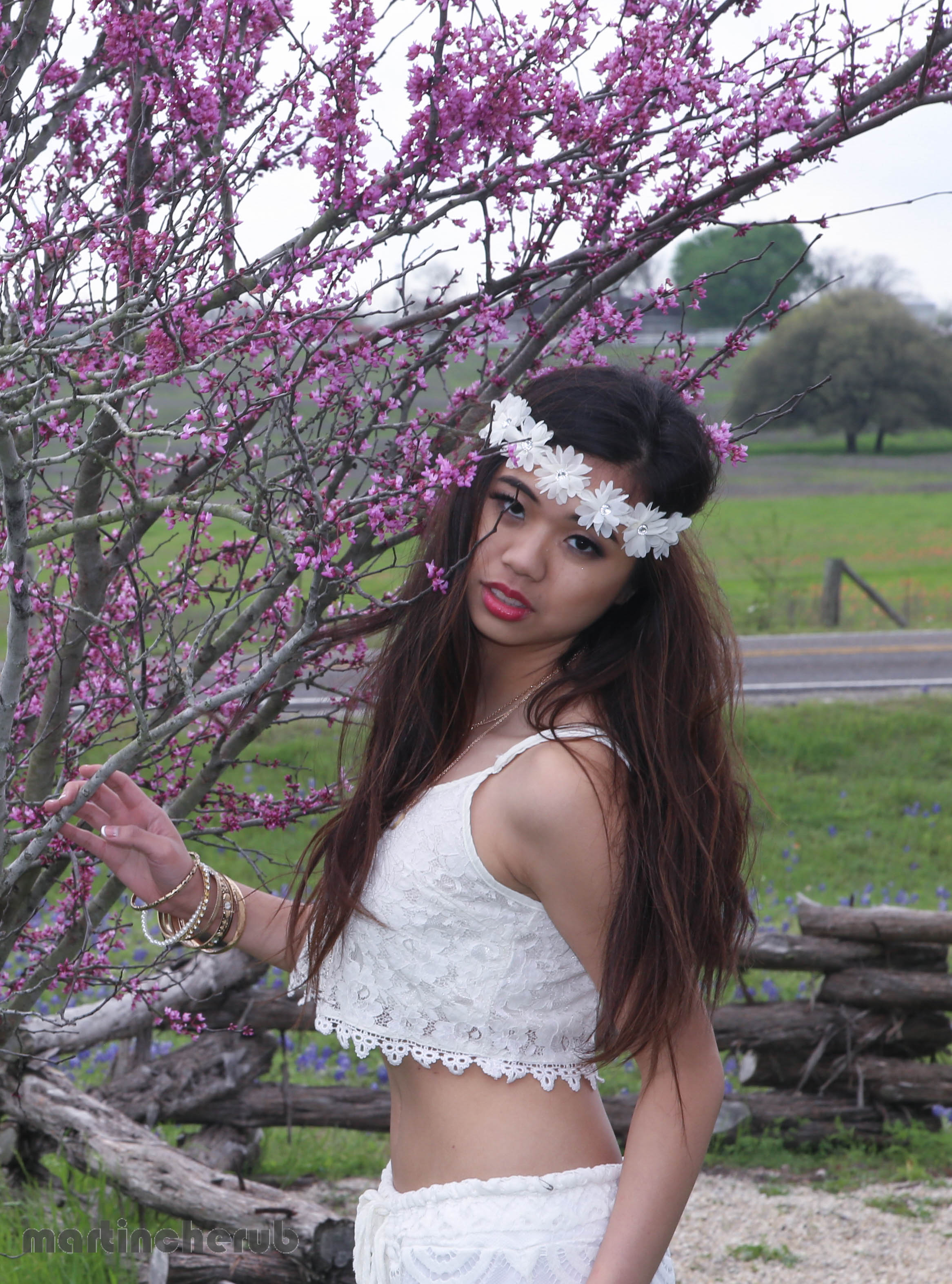 Tiffany beside a blooming Texas redbud tree, with bluebonnets in the background