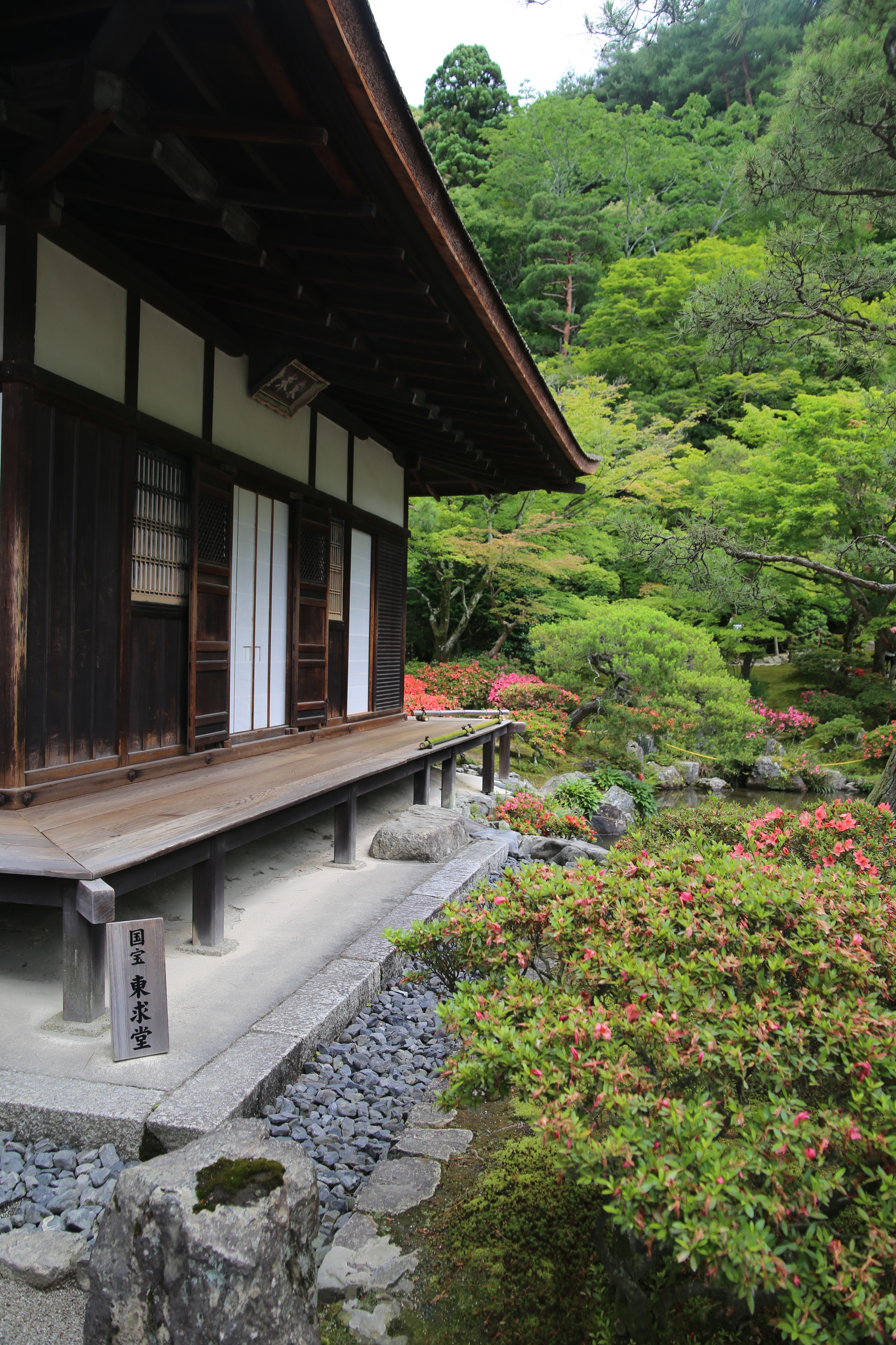 Side view of a temple building with a stone walkway and azalea bushes in bloom