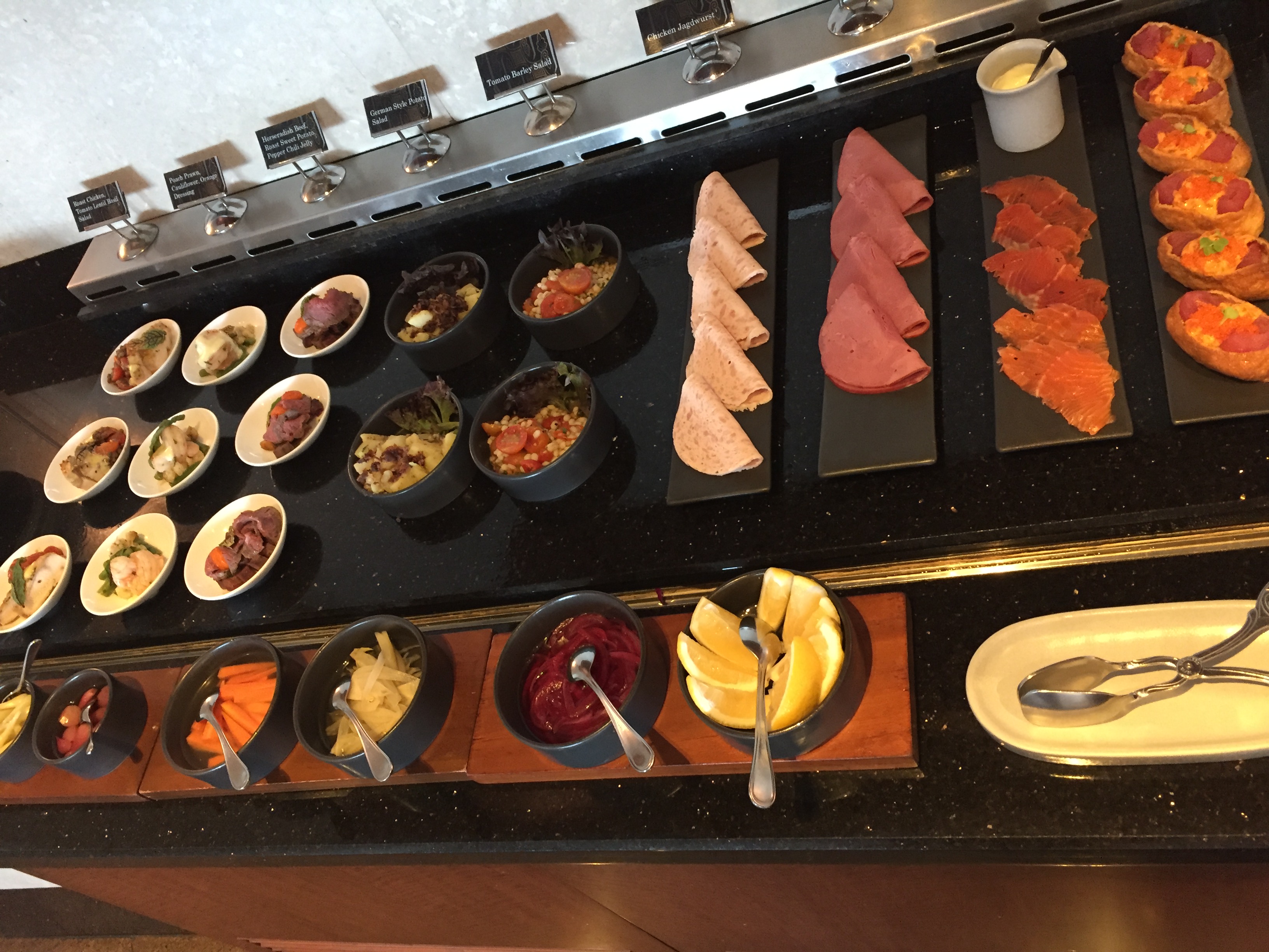 A long lacquered counter with sushi, charcuterie, salmon, ham, and bread arrayed across stations