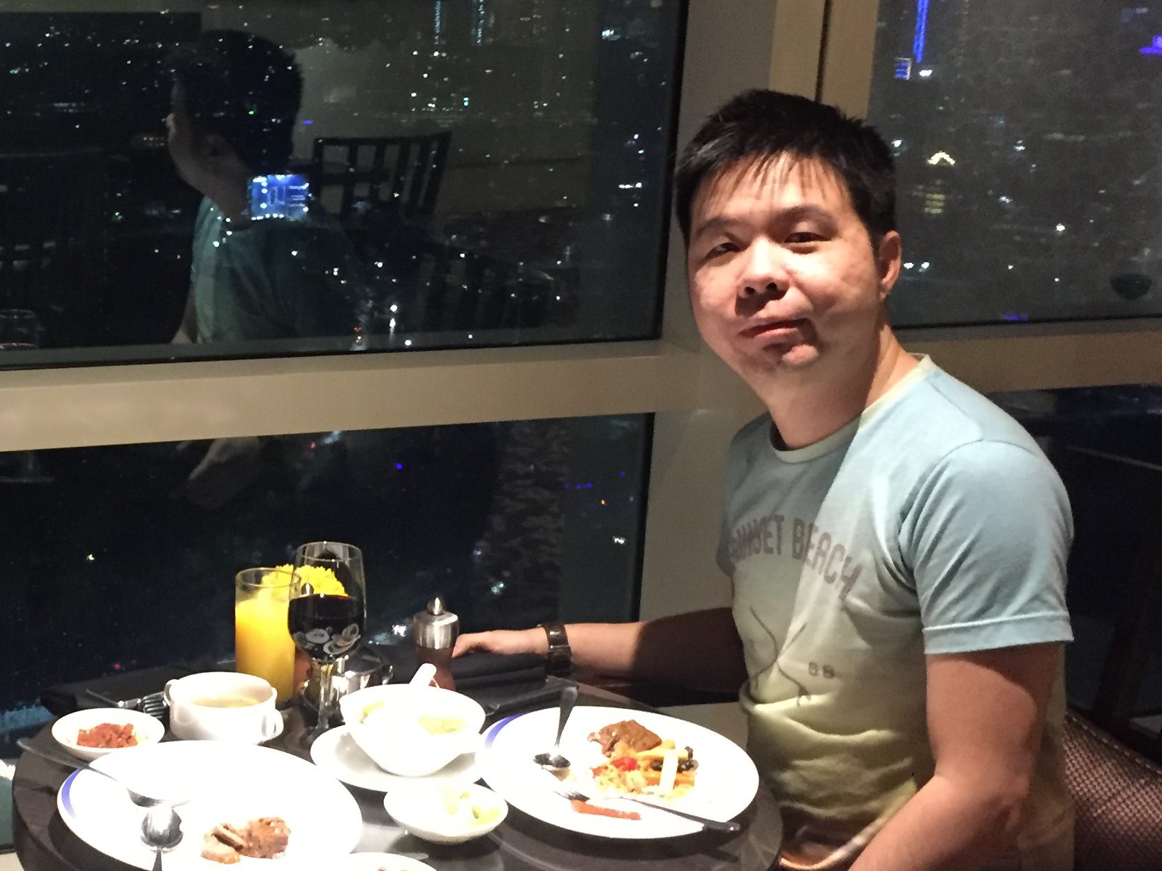Martin Cherub seated at the lounge with a plate of food and the night view of Jakarta visible through floor-to-ceiling windows