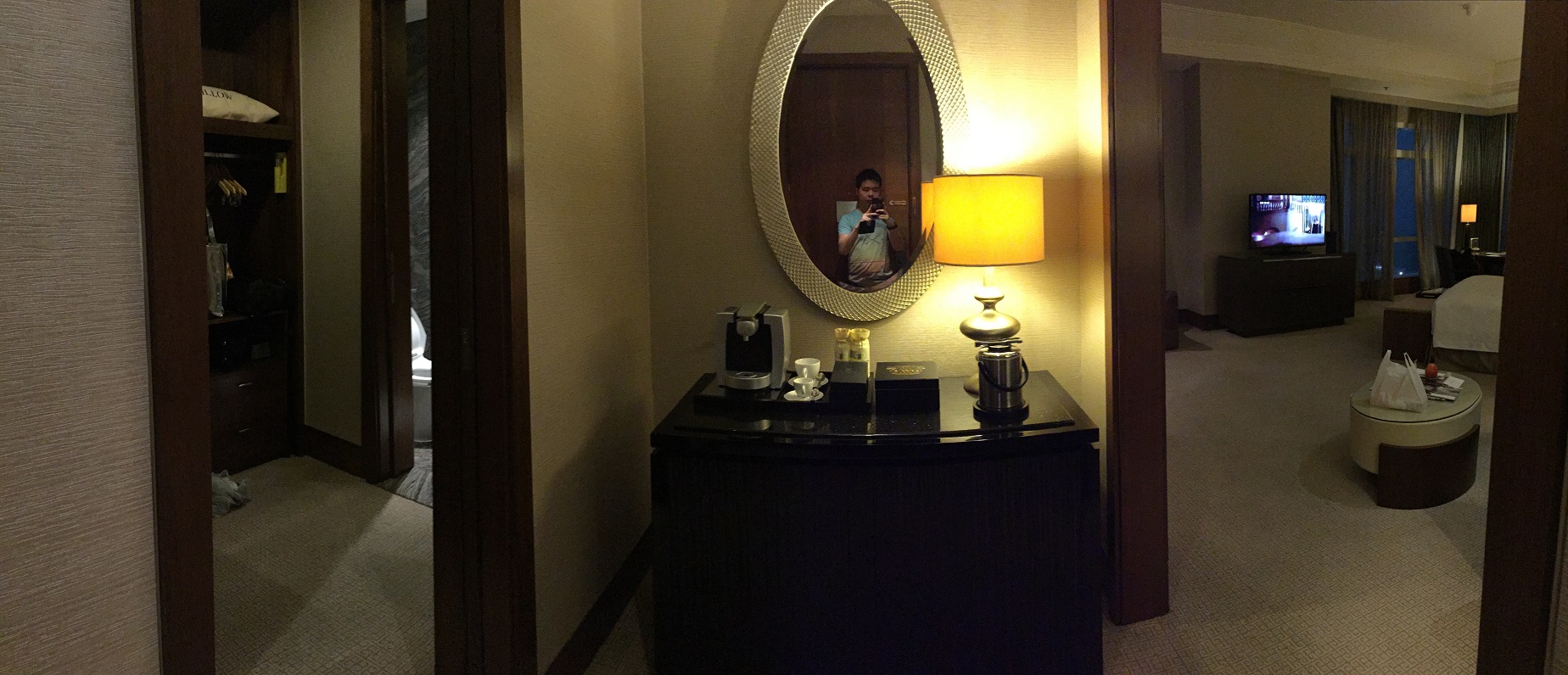 Corner of the suite — a curved console with a dressing mirror, lamp, and Nespresso machine, with the bedroom visible through doorways