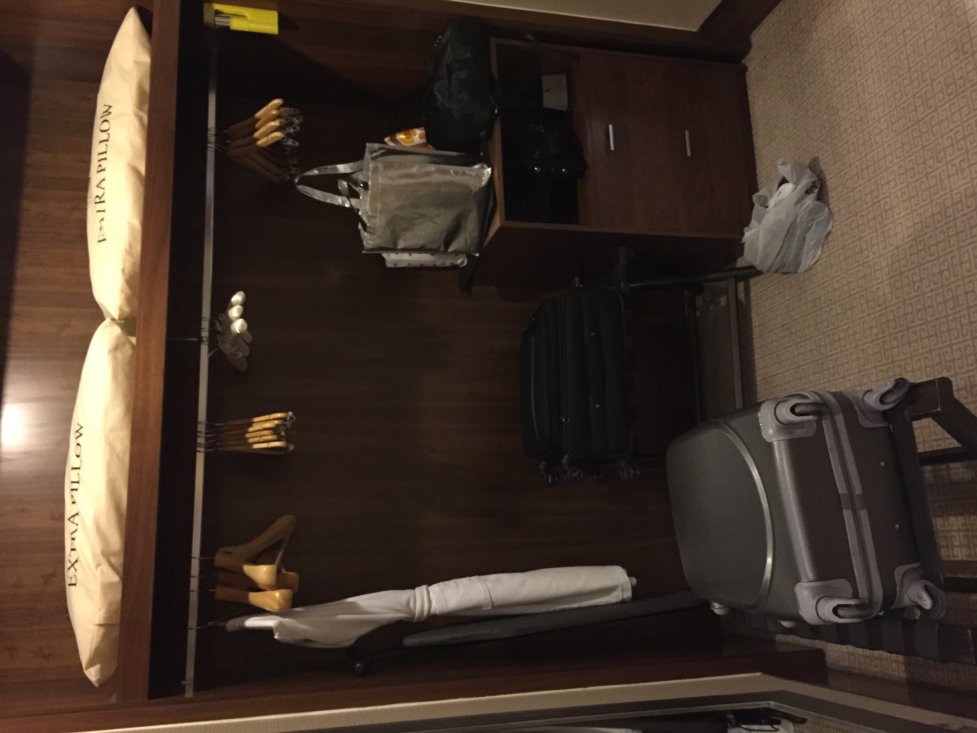 A spacious walk-in closet with hanging garment bags, suitcases, and an "Extra Pillow" tag visible on a stored pillow