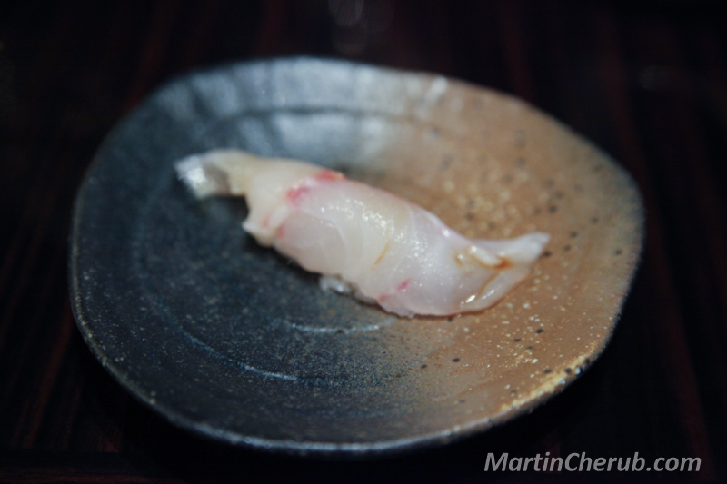 Pale, translucent nigiri on a dark plate