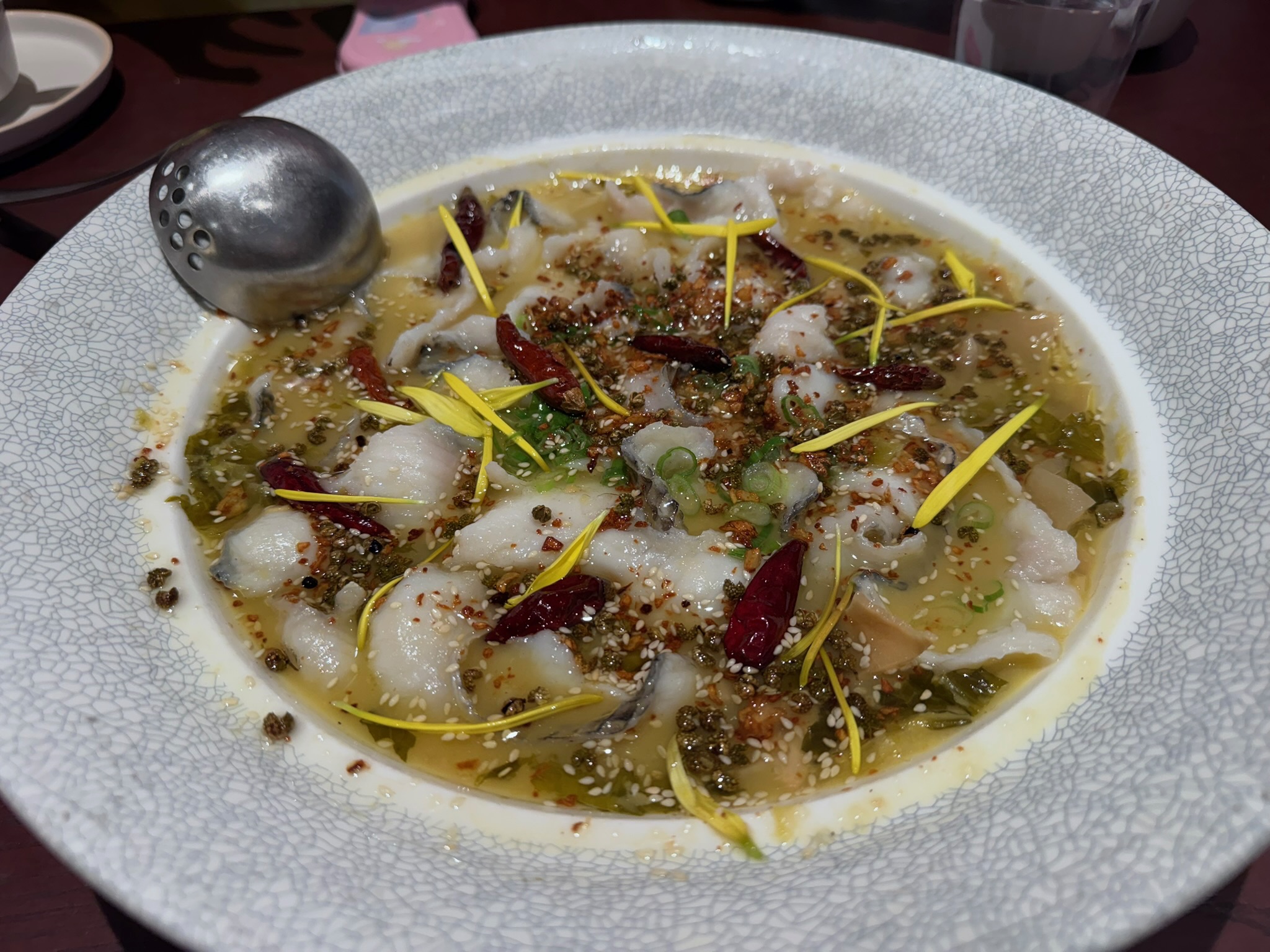 Tai Er's signature Sichuan sauerkraut fish — sliced fish in a tangy broth with pickled mustard greens, dried chilies, and yellow flower garnish