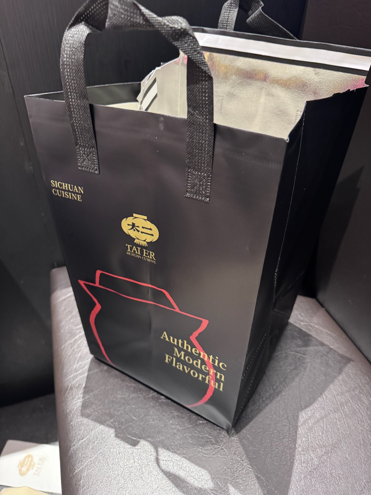 A black take-out bag with the Tai Er logo and "Authentic Modern Flavorful" text in gold